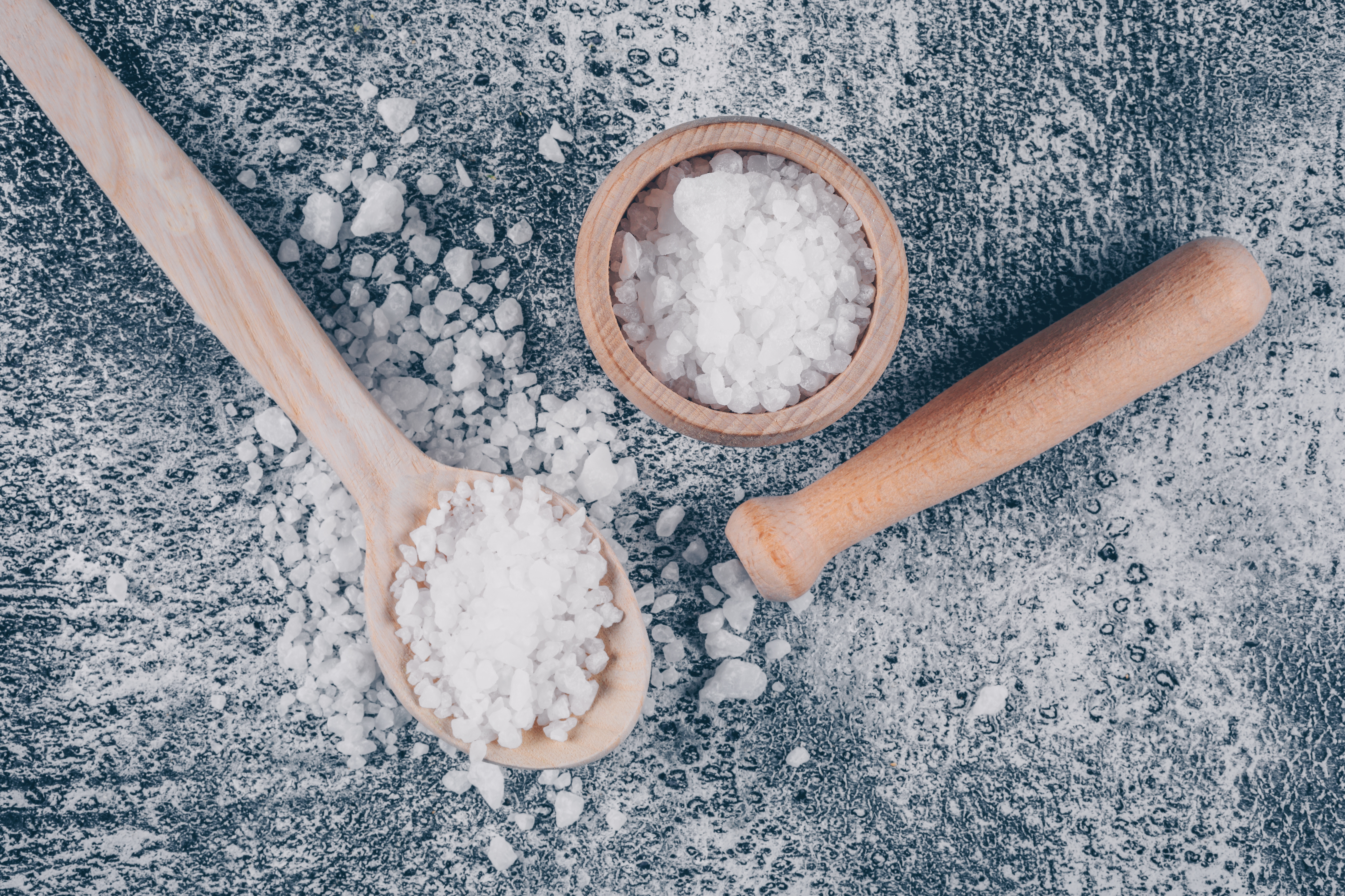 Sea salt in a bowl and spoon with rolling pin top view on a gray textured background